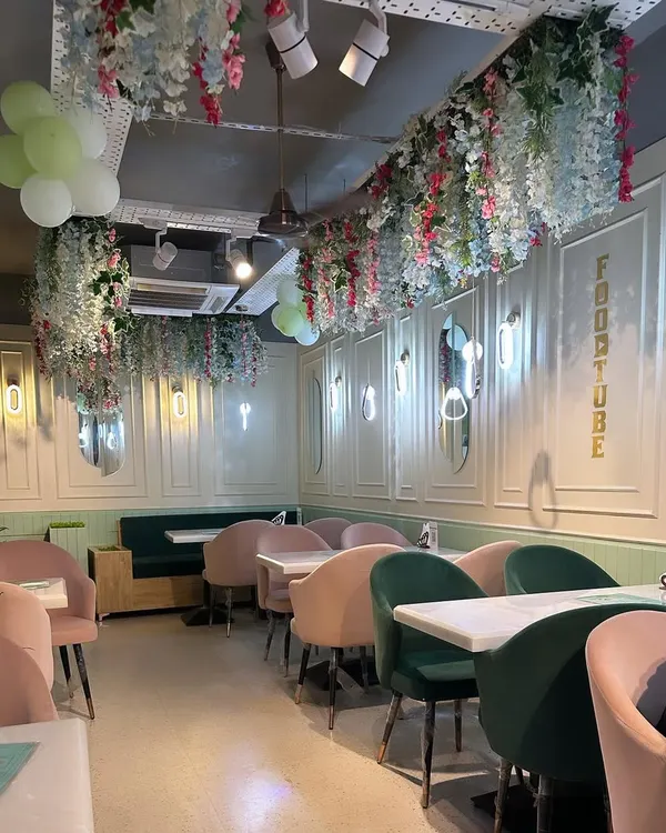 The interior of a restaurant in GK 1, featuring a pastel color scheme with pink and green chairs. I used wall molding and floral ceiling installations to create a whimsical and charming dining atmosphere.