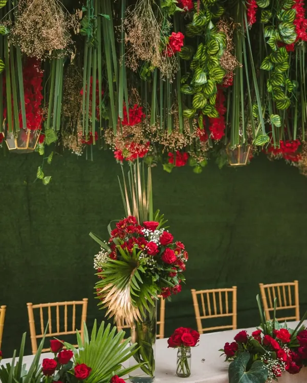 A tablescape that is a work of art. We designed this setting with a dramatic overhead installation of hanging red flowers and greenery, complemented by lush red floral centerpieces on the table below.
