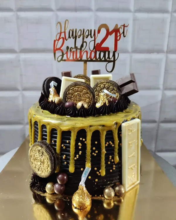 A stunning 21st birthday chocolate overload cake. This design features a rich chocolate drip, golden Oreos, Hershey's Kisses, and other assorted chocolates for a truly decadent celebration.