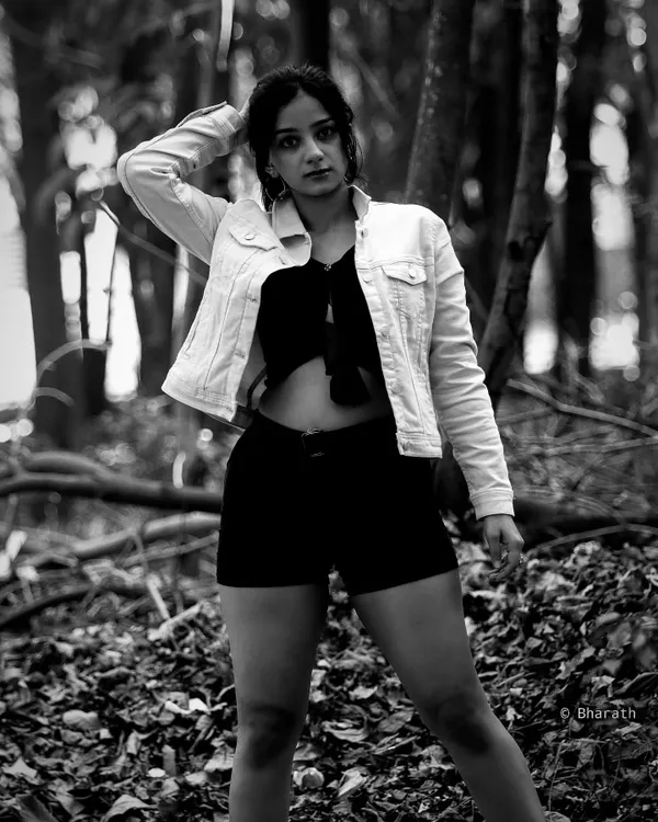 A powerful black and white portrait in a forest setting. The monochrome tones emphasize the texture of the leaves and the subject's confident stance.
