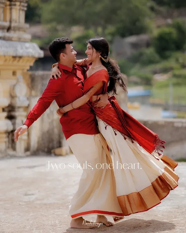 A couple shares a joyful, spontaneous dance at Melukote, their traditional red and white outfits flowing with the movement. This is a perfect example of capturing unposed happiness against a historic backdrop.