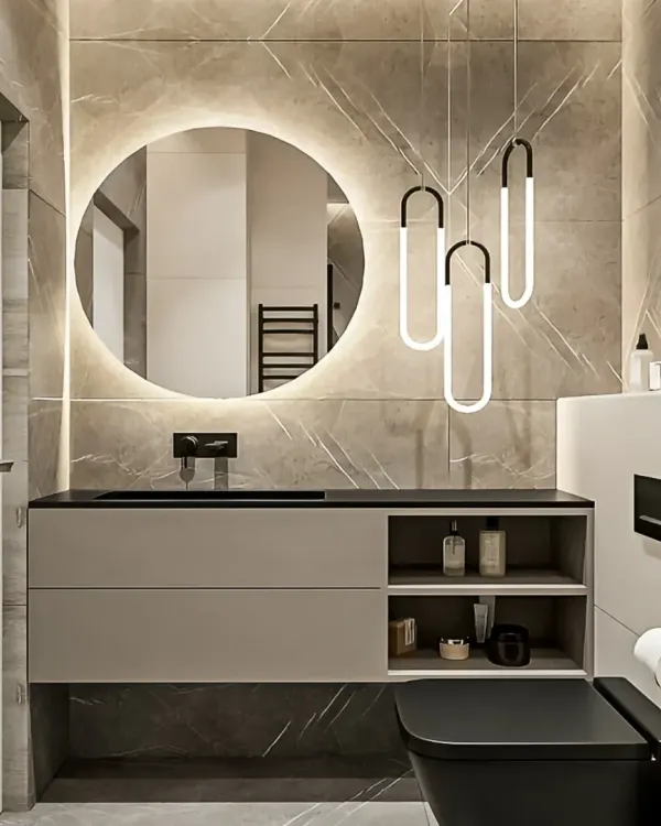 A chic and modern bathroom featuring a floating vanity with open and closed storage. The large, backlit circular mirror and stylish pendant lights add a touch of glamour to the marble-tiled space.