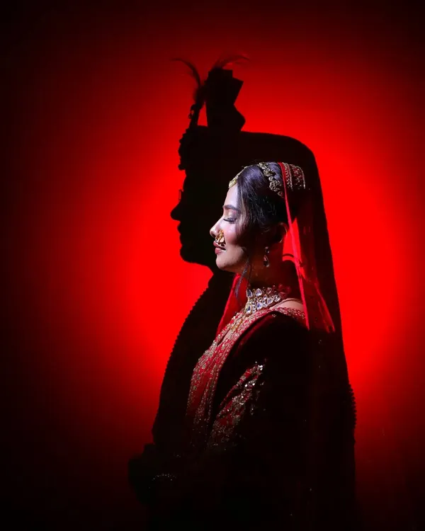 A creative silhouette of the bride, with the groom's shadow cast upon a bold red background. We love using shadows and light to create dramatic, artistic portraits like this one.