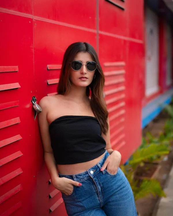 A classic street style portrait. The model's simple black tube top and jeans pop against the vibrant red industrial background, creating a look that is both cool and confident.