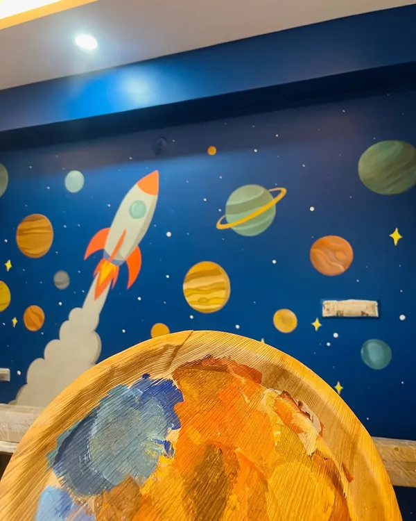 A work-in-progress shot of the solar system mural. You can see my paint palette in the foreground, filled with the cosmic colors used to bring the planets and rocket ship to life on the deep blue wall.