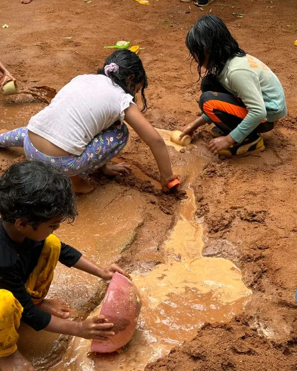 Children work together to dig channels and create rivers in the mud pit on a rainy day. This is collaborative, sensory play at its best.