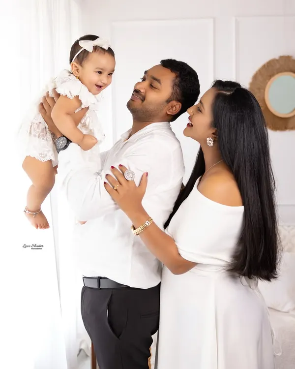 A picture-perfect family moment. The joy is contagious as this mom and dad lift their laughing baby girl, all dressed in coordinating white outfits.