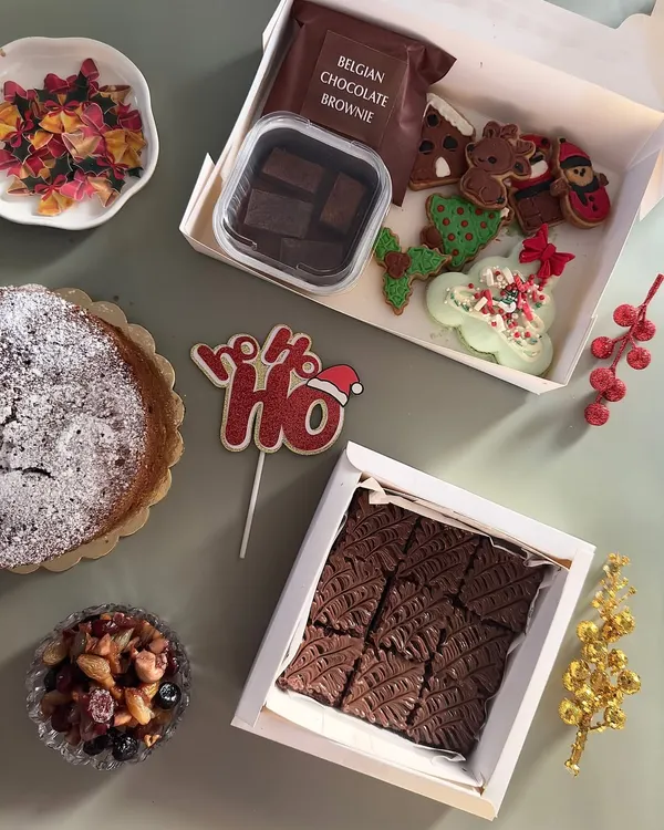 My Christmas goodie box is filled with holiday magic. It contains a variety of festive treats, including hand-decorated sugar cookies, a Belgian chocolate brownie, and a macaron wreath.