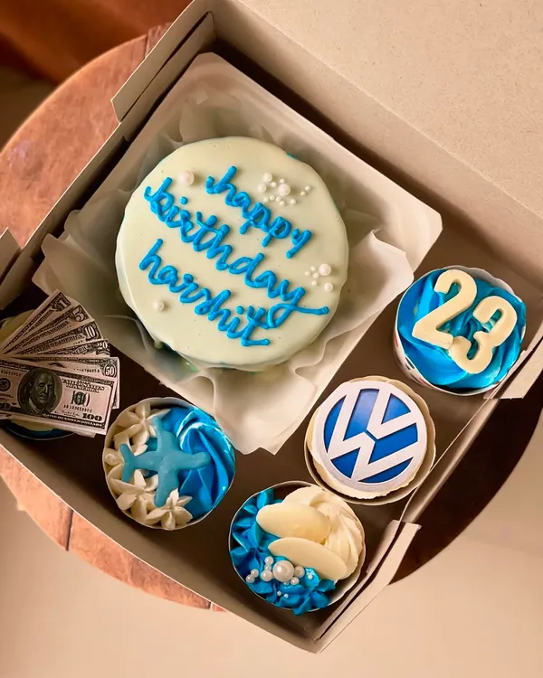 This custom bento and cupcake combo is a perfect example of a themed birthday set. The light blue cake with "happy birthday" script is paired with four cupcakes, each decorated with unique toppers like the Volkswagen logo, a number 23, and beach-themed elements, showing how we can personalize a gift for any interest.
