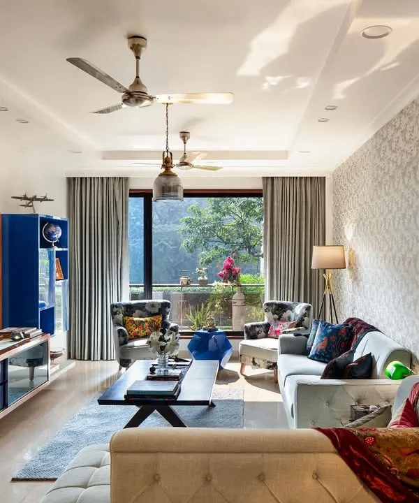The living room at Ridge View, where botanical print wallpaper mirrors the greenery outside. We used soft blue sofas and curated lounging chairs to create a sanctuary for quiet moments, with a striking deep blue shelf housing books and memorabilia.
