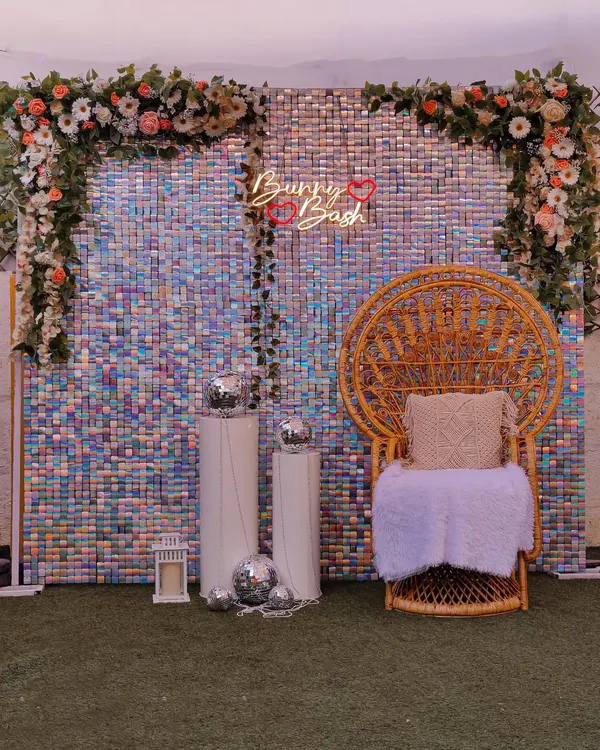 A glamorous sequin backdrop with a peacock chair. This iridescent wall is perfect for a baby shower, haldi, or mehendi, and can be customized with a neon sign and floral arrangements.