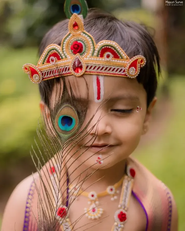 A creative portrait of a little boy dressed as Krishna, playfully peeking from behind a peacock feather. This shot highlights the artistic details of my themed kids' photoshoots.