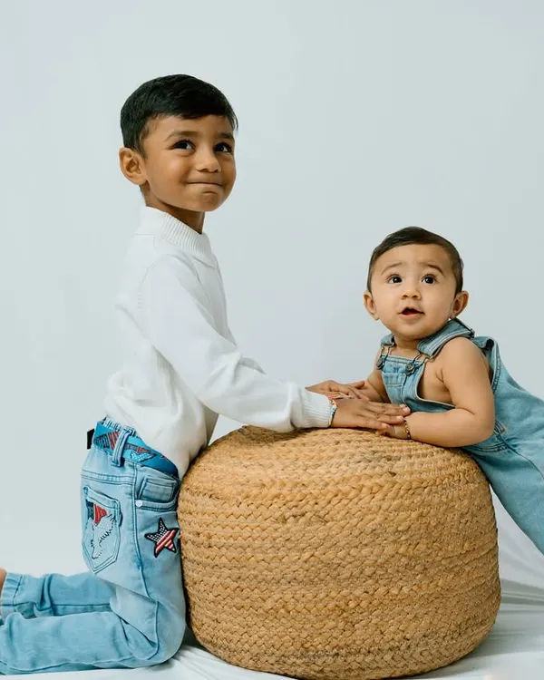 A classic studio portrait of two brothers. The older brother rests his hand gently on a stool where his baby brother is propped up, a sweet image of their budding friendship.