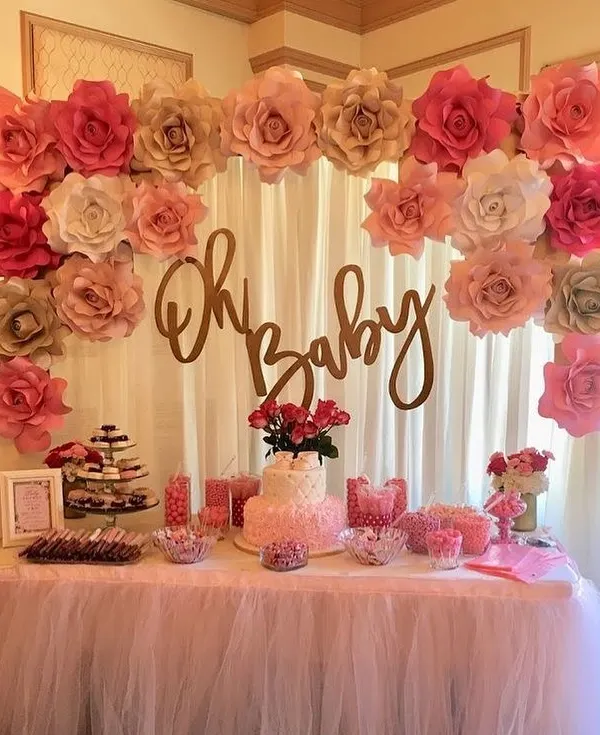 A classic "Oh Baby" shower theme with a beautiful dessert table. The backdrop features a curtain of paper flowers in shades of pink and gold, creating a sweet and celebratory setting.