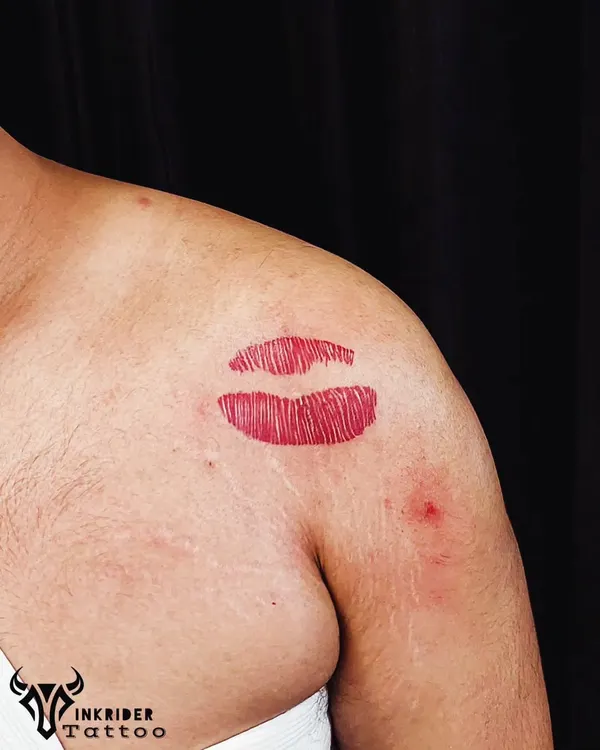 A vibrant red lipstick kiss tattoo on the shoulder. This is a fun, bold, and playful piece that makes a statement.
