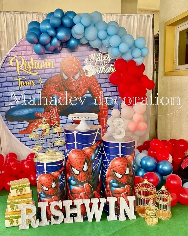 An action-packed Spiderman theme for a third birthday. This setup features a large circular backdrop with a brick wall and Spiderman graphic, themed pedestals, and a red and blue balloon arrangement.