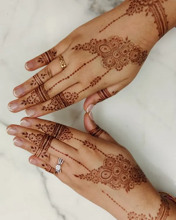 A stylish and minimal Arabic design, perfect for an engagement party guest. The pattern flows diagonally across the back of the hand, with simple bands on the fingers.