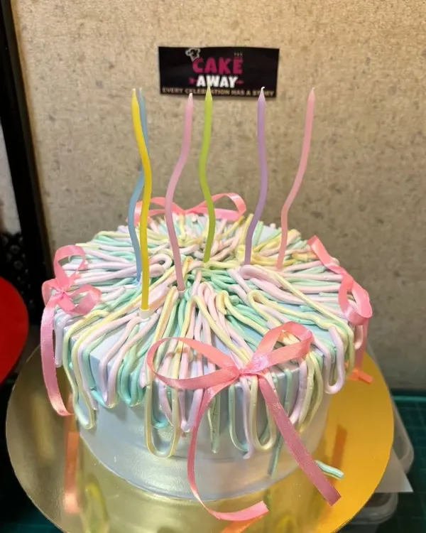A trendy pastel ribbon cake. This design uses piped buttercream in multiple colors to create a beautiful, flowing ribbon effect, topped with whimsical candles.