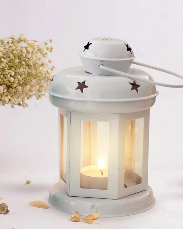 This white metal lantern is a charming holder for a single tealight candle. It protects the flame while casting a gentle, starry pattern of light, perfect for indoor or outdoor decor.