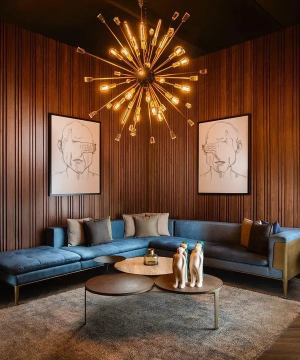We created this luxurious living room with a moody and sophisticated palette. The space is anchored by our custom blue sectional sofa and layered coffee tables, all framed by warm, vertical wood paneling and a striking sputnik chandelier.