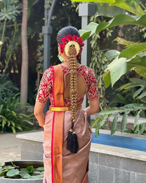 A classic South Indian bridal look, featuring an intricate poola jada braid adorned with traditional temple jewelry and fresh red roses. This style is a testament to timeless elegance and is one of my signature offerings for brides.