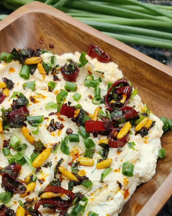 Our creamy Whipped Pinenut Feta dip, generously topped with sun-dried tomatoes, toasted pine nuts, and fresh spring onions. It's perfect with crackers or grilled vegetables.
