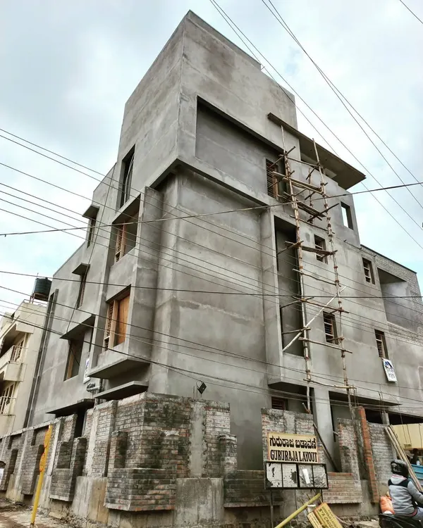 A residential building in Giriraja Layout, shown with its final plastering complete. The raw concrete form is celebrated, showcasing the building's strong, sculptural lines before the final paint and finishes are applied.