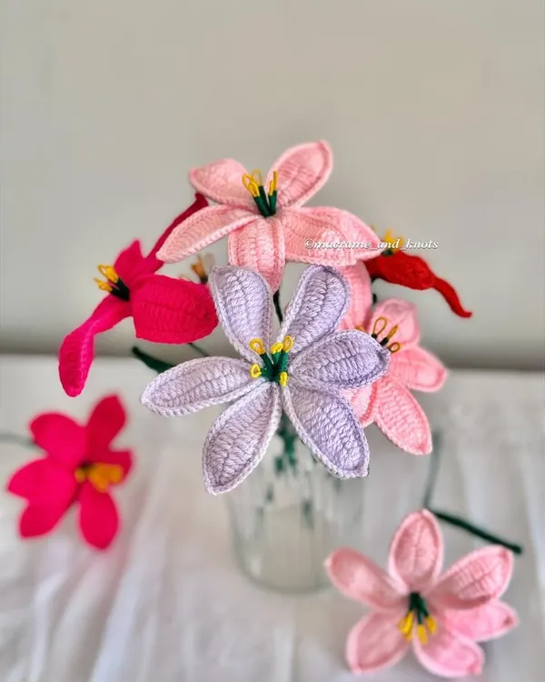 I'm so excited to launch my new crochet lily flowers. This photo shows them in four different shades: baby pink, vibrant pink, lavender, and red, displayed in a simple glass.