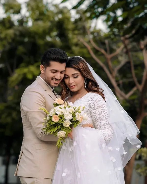 A gentle moment between a bride and groom after their Catholic wedding ceremony, captured outdoors. The bride's white gown and veil are beautifully highlighted.