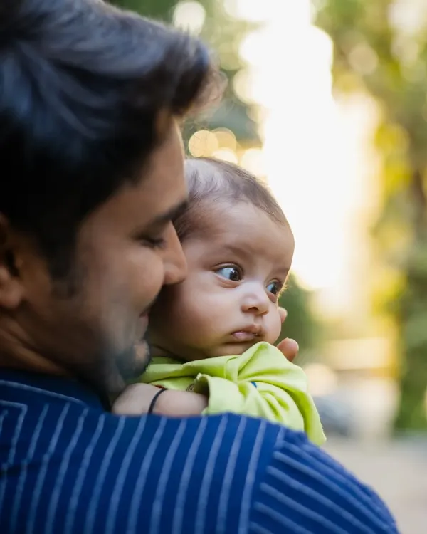 A heartwarming shot of a father holding his newborn baby over his shoulder. The baby's curious expression and the soft outdoor light make this a precious memory.