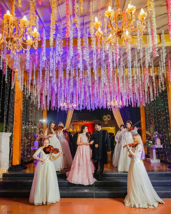 A fairytale entrance for the couple, flanked by violinists under a canopy of hanging flowers. We specialize in capturing these grand, cinematic moments that make your event unforgettable.