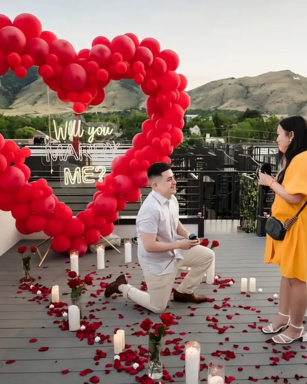 The perfect moment captured. We set the stage for a lifetime of memories with this rooftop proposal, featuring a giant red balloon heart, a "Will you marry me?" neon sign, and a romantic pathway of candles and rose petals.