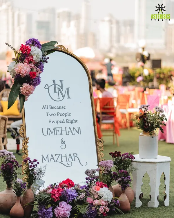 A modern and romantic welcome sign for a Mehendi. We combined a chic mirror with a beautiful floral arrangement and a playful quote, "All Because Two People Swiped Right," to personalize the entrance.