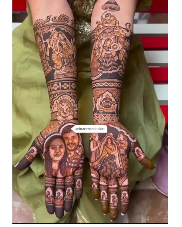 A truly personalized bridal mehandi featuring realistic portraits of the couple on one palm. The other hand and arms depict a full wedding story with Radha-Krishna, Lord Ganesha, and baraat procession elements.
