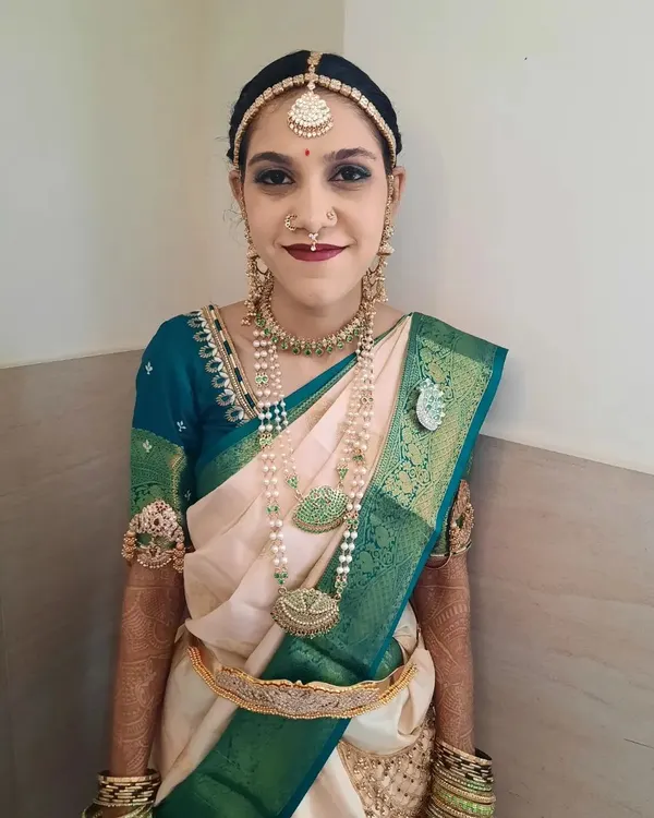A full portrait of Bride Shalini for her Muhurtham. The makeup features a bold lip and striking eye makeup that beautifully complements her traditional off-white and green silk saree and antique-finish jewellery.