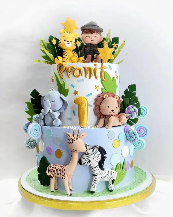 A beautiful two-tier cake for a first birthday, featuring a whole family of cute, hand-molded jungle animals and a little boy figurine.