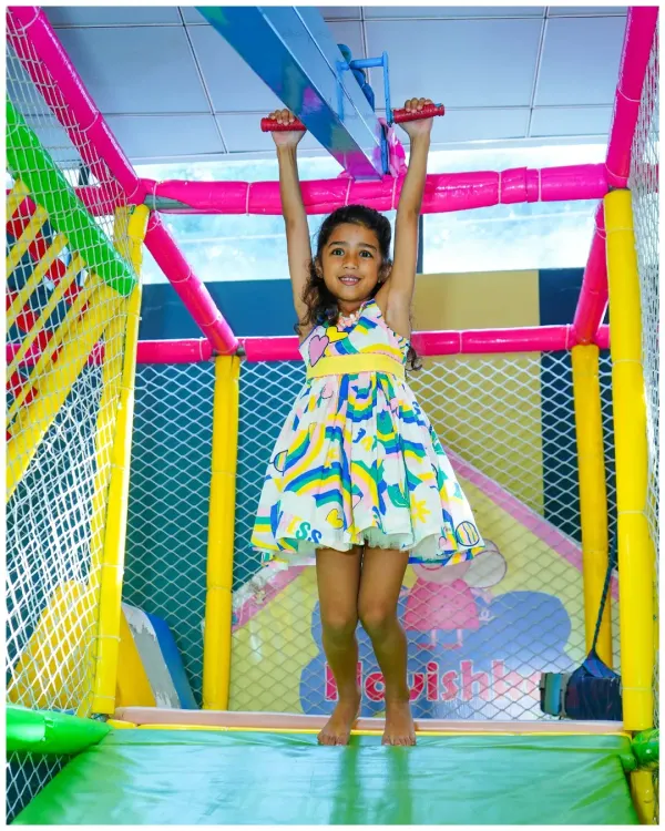 A happy child confidently navigates the monkey bars in our colorful indoor play gym. The entire structure is padded and enclosed with safety netting.
