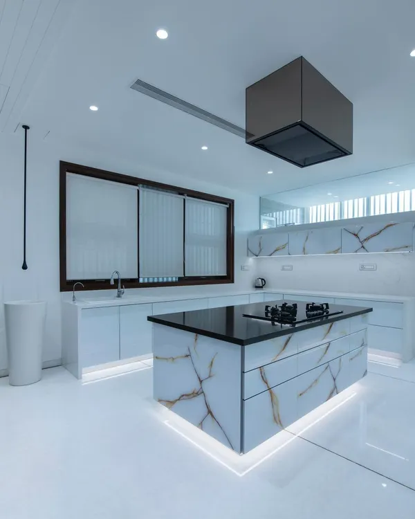 A stunning example of a modern minimalist kitchen, featuring a monolithic island wrapped in book-matched porcelain with gold veining. Under-cabinet and island lighting adds a floating effect to the clean, all-white design.