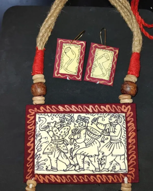 This rectangular pendant necklace is my tribute to the Kalighat and Jamini Roy style of painting. The piece depicts a festive scene with musicians, hand-drawn on a fabric base and framed in deep red. The set includes matching earrings, all crafted to be lightweight and culturally rich.