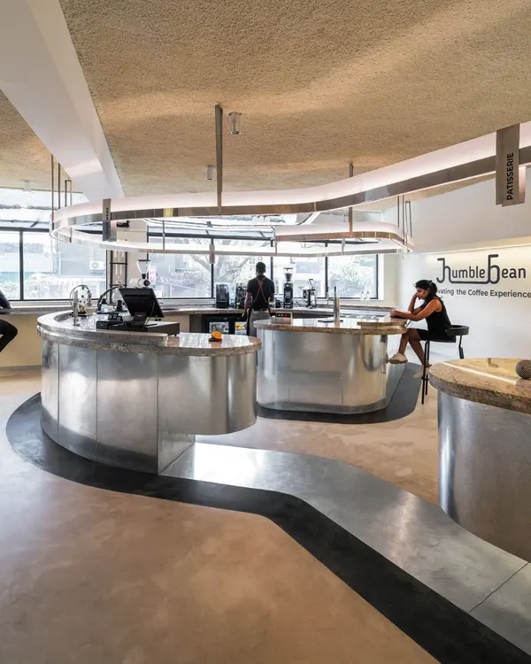 At Humble Bean in Bengaluru, the entire interior is a sensory experience designed to mirror a perfect cup of coffee. This view highlights the monolithic, bean-shaped brew bar that meanders through the space, guiding movement and putting the craft of coffee making on theatrical display.