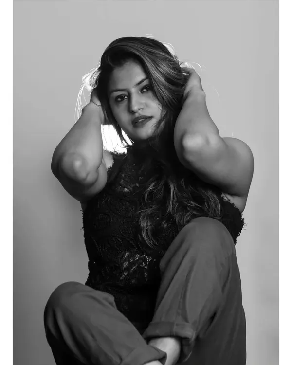A powerful black and white studio portrait. The strong contrast and backlighting create a dramatic halo effect around the model's hair, while her pose conveys confidence and intensity.