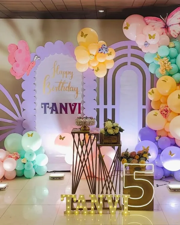 A beautiful pastel butterfly theme for a 5th birthday, featuring a custom backdrop, marquee letters, and large butterfly wing cutouts.