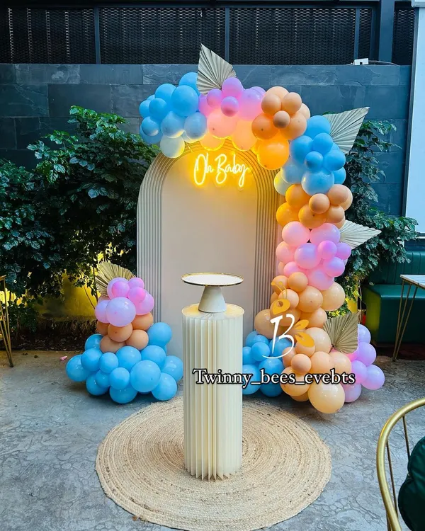 A trendy boho-style baby shower setup. We used a modern arched backdrop with an "Oh Baby" neon sign, surrounded by a beautiful balloon arrangement in pastel blue, pink, and orange.
