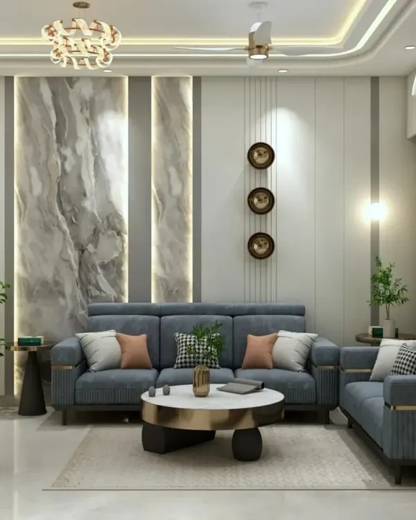 A luxurious living room featuring a grey marble-patterned accent wall with integrated vertical lighting. The plush blue sofa set and gold-accented coffee table create a sophisticated space for entertaining.