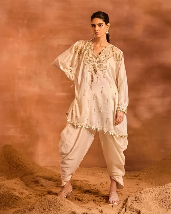 The Orion Kaftan Set in a classic ivory. This ensemble features a stunningly embellished kaftan with phoenix-inspired motifs and pearl tassels, paired with comfortable and stylish solid dhoti pants.