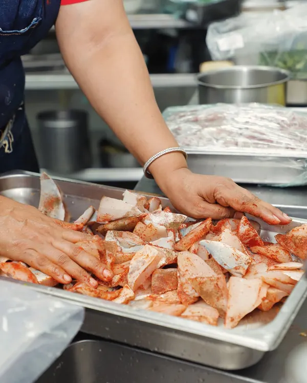 There is nothing better than using bare hands to create, enhance, and elevate a dish. Here, I am marinating fresh fish, ensuring every piece is coated with our special masala mix. This hands-on approach is the essence of our homestyle cooking.