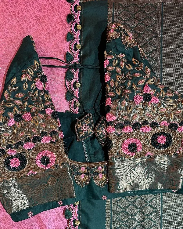 This is a close-up of a dark green blouse we designed to pair with a pink saree. It features beautiful floral embroidery using pink, gold, and black threads, with unique circular motifs that add a modern touch.