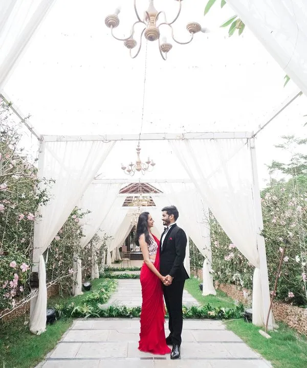 A breathtaking moment captured under a canopy of white drapes and chandeliers. This shot perfectly frames the couple's elegant attire and the promise of their future, creating a truly cinematic and romantic pre-wedding photograph.