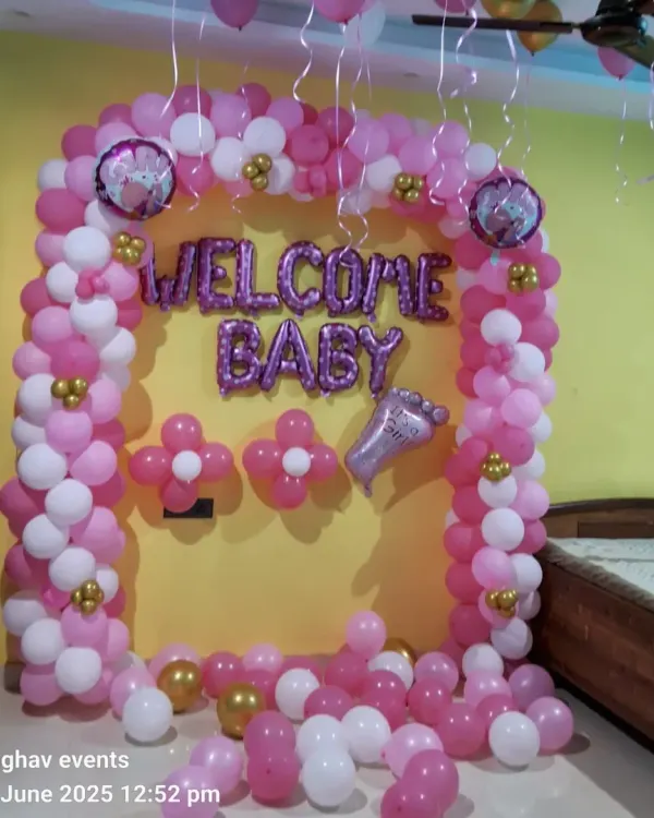 A classic "Welcome Baby" decoration for a girl. This setup includes a pink and white balloon arch, "WELCOME BABY" foil letters, and small gold balloon accents.