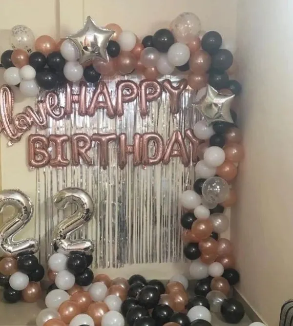 A popular room decoration setup for a 22nd birthday. This features a silver foil curtain, "Happy Birthday" and "love" foil letters, and a balloon arch in rose gold, black, and white.
